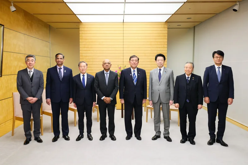 Eight people in business suits stand in a row for a formal photo at the Japanese prime minister's office, with Arvind Krishna fourth from the left next to Prime Minister Shigeru Ishiba