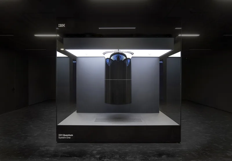 IBM Quantum System One, a quantum computer housed in a tall glass cube, on display in a dark room in Germany