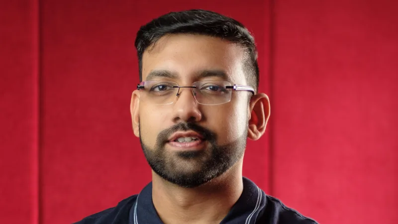 Shashank Kumar, Razorpay co-founder, in rimless glasses and a navy collared T-shirt against a red padded wall