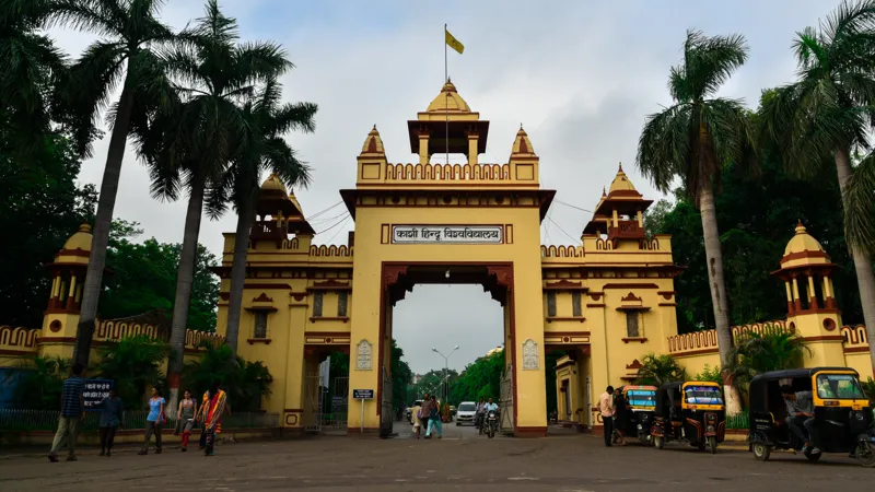 The main gate of Banaras Hindu University in Varanasi with an arched entrance, pedestrians and auto-rickshaws