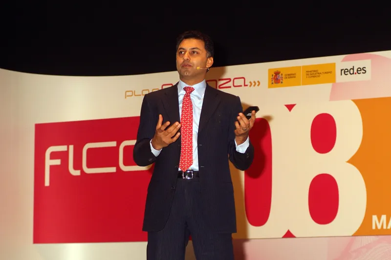 Nikesh Arora in a suit and red tie gesturing on stage in front of a large FICOD 08 backdrop