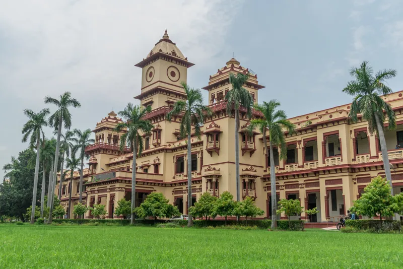 The domed sandstone building of the Department of Electrical Engineering at IIT (BHU) Varanasi, with palm trees and a lawn in front