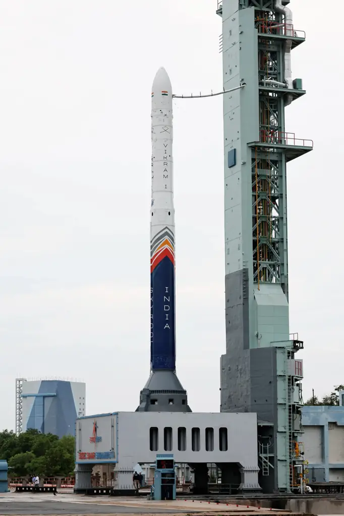Skyroot's Vikram-I rocket, white with a blue and orange lower stage marked INDIA, standing beside the launch tower at Sriharikota